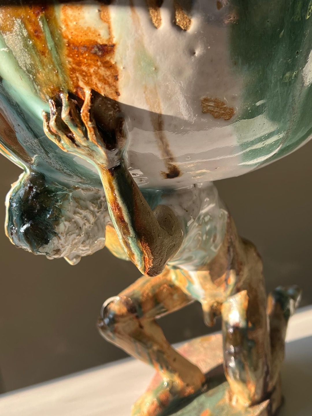 Detail of a stoneware sculpture, an Atlas holding up the world, house glaze drips running upward